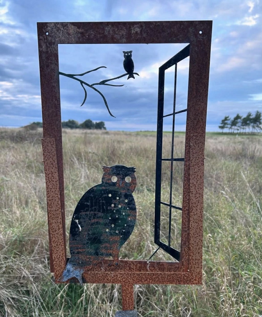 Bild på metallfönster med en uggla i öppet fönster som leder mot grönhögen
